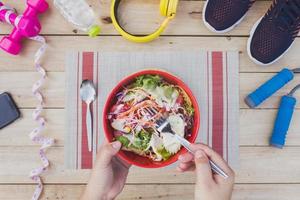 Jeune femme en mangeant fruit salade ensemble avec aptitude équipement. photo