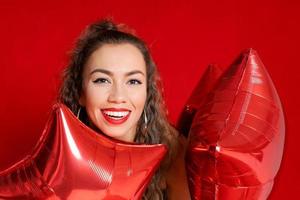 souriant content caucasien fille dans noir robe avec rouge des ballons dans forme étoiles photo