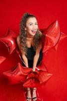 souriant content caucasien fille dans noir robe avec rouge des ballons dans forme étoiles photo