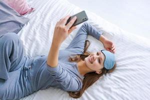 content Jeune femme relaxant en utilisant et parlant avec téléphone intelligent sur lit à Accueil photo