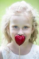 peu fille en portant une petit rouge cœur. enfant avec une jouet cœur. photo