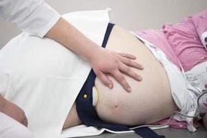 une Enceinte femme visites une gynécologue dans le champ de médicament ou médicament pour une grossesse consultant. le médecin examine le ventre de une Enceinte femme. photo