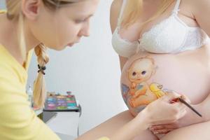 Jeune maquillage artiste dessine une bébé sur le ventre photo