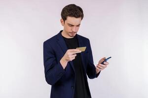 portrait de malheureux Jeune homme d'affaire permanent en utilisant mobile cellule téléphone et en portant crédit banque carte isolé sur blanc Couleur Contexte studio photo