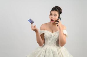 Jeune asiatique magnifique la mariée affectation avec crédit carte et téléphone intelligent dans main photo