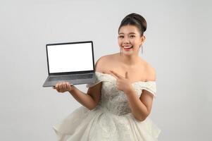 Jeune belle mariée asiatique pose avec un ordinateur portable maquette à la main photo