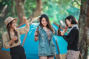 les jeunes femmes applaudissent et boivent une boisson devant la tente de camping photo