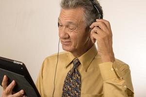 plus âgée homme écoute à la musique ou une Podcast portant tête téléphone sur le sien intelligent tablette photo