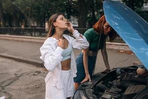 deux femmes avec une voiture cassée sur la route. capot ouvert photo