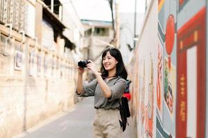 Jeune asiatique femme sac à dos voyageur en utilisant numérique compact caméra, profiter rue culturel local endroit et sourire. voyageur vérification en dehors côté des rues. photo