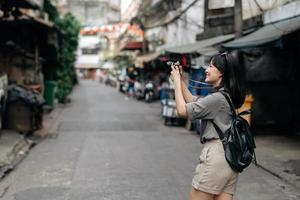 Jeune asiatique femme sac à dos voyageur en utilisant numérique compact caméra, profiter rue culturel local endroit et sourire. voyageur vérification en dehors côté des rues. photo
