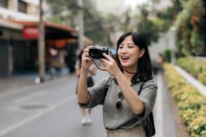 Jeune asiatique femme sac à dos voyageur en utilisant numérique compact caméra, profiter rue culturel local endroit et sourire. voyageur vérification en dehors côté des rues. photo