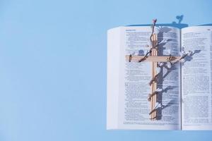 croix décorée de fleurs avec la sainte bible sur fond bleu. concept minimaliste de vacances de pâques photo