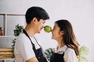 dans cuisineparfaitement content couple en train de préparer en bonne santé nourriture, beaucoup de des légumes. homme jongle avec des fruits, fait du sa petite amie rire. charmant gens dans l'amour avoir amusement photo