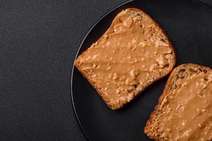 nutritif sandwich qui consiste de pain et cacahuète beurre sur une noir céramique assiette photo