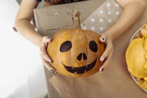 enfant en portant Halloween citrouille jack o'lanterne. Halloween fête concept. peu fille dessin effrayant visage avec peindre brosses avec Parents sur citrouille pour maison décoration. sélectif concentrer photo