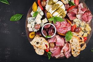 antipasto plat avec jambon, prosciutto, salami, bleu fromage, mozzarella avec Pesto et Olives sur une en bois Contexte. Haut voir, aérien photo