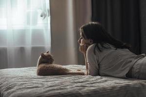 une belle jeune fille en pyjama se trouve sur un lit à la maison, à côté de son chat britannique pêche photo