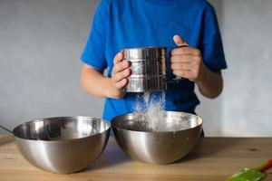 une enfant prépare pâte dans métal boules. tamiser le farine. mains photo