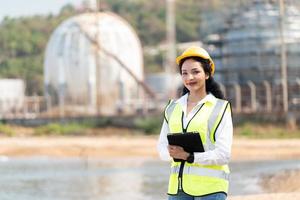 femelle ingénieur avec casque avec pétrochimique usine Contexte. asiatique femme en portant tablette, plan et walkie parlant. photo