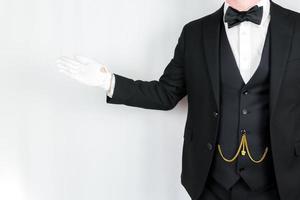 portrait de majordome dans foncé costume et blanc gants permanent avec accueillant geste. concept de un service industrie et professionnel hospitalité. photo