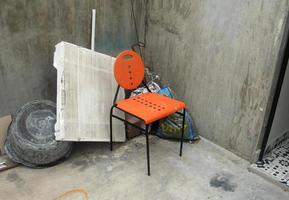 Ouest Djakarta, Indonésie - février 18ème, 2023 - Facile Orange bureau étude chaise isolé sur gris ciment béton des murs et étages. noir seau et blanc polystyrène objet sur le Contexte. photo