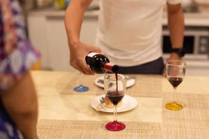 mari verser rouge du vin dans verre de épouse pendant dîner à maison. photo