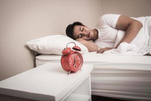 homme dort dans son lit avec réveil rouge photo