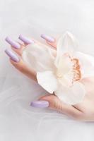 les mains de la fille avec une délicate manucure violette et des fleurs d'orchidées photo