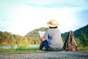 une femme asiatique âgée porte un chapeau assis sur l'herbe pour voir une carte du tourisme de nature. le concept de tourisme de santé pour les personnes âgées photo