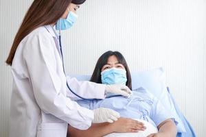 médecins utilisé une stéthoscope à examiner le santé de une graisse femme, portant une masque, mensonge sur une hôpital lit. traitement de les patients pendant le coronavirus épidémie. concept de médical service. copie espace photo