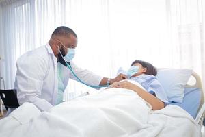 un médecin afro-américain vérifie la maladie d'une femme allongée dans un lit d'hôpital. traitement des patients pendant l'épidémie de coronavirus. concept de service médical. photo