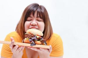 graisse asiatique femmes manger grand hamburger, blanc Contexte. santé concept. gens qui sont en surpoids. photo