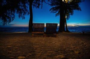 en bois chaise à côté de le plage avec magnifique idyllique paysage marin le coucher du soleil vue sur kohkood island.koh bien, aussi connu comme ko kout, est un île dans le golfe de Thaïlande photo