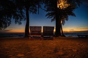 en bois chaise à côté de le plage avec magnifique idyllique paysage marin le coucher du soleil vue sur kohkood island.koh bien, aussi connu comme ko kout, est un île dans le golfe de Thaïlande photo