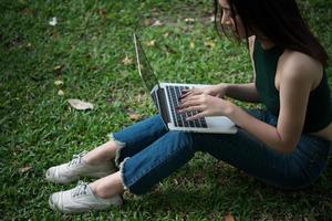 Belle jeune femme assise sur l'herbe verte et utilisant un ordinateur portable dans le parc photo