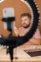 homme vlogging à propos faire en haut et beauté des produits. Masculin tournage une maquillage Didacticiel. gars enseignement faire en haut Didacticiel en utilisant sa téléphone - la diversité et blogueur concept. photo