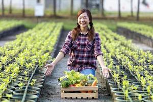 asiatique femme agriculteur est montrant le en bois plateau plein de fraîchement choisir organiques des légumes dans sa jardin pour récolte saison et en bonne santé régime nourriture photo