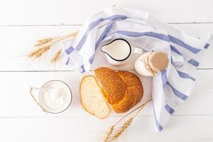 Frais laitier des produits, une pain de pain, une bouquet de oreilles de blé pour le fête de juif chavouot. Haut voir. en bois blanc Contexte photo