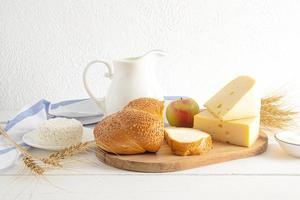 une grand cruche de lait, haché pain, fromage, chalet fromage sur une Coupe planche. de face voir. traditionnel laitier des produits pour le vacances de chavouot. photo