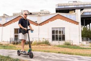 banlieusard branché homme est en utilisant électrique scooter sur le faubourgs de une ville photo