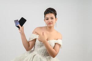 Jeune asiatique magnifique la mariée affectation avec crédit carte et téléphone intelligent dans main photo