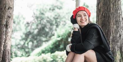 portrait de content asiatique Jeune femme séance sur une pelouse en dessous de une arbre dans parc photo