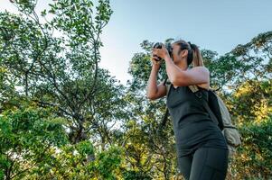 une jeune femme routarde utilise un appareil photo pour prendre des photos en forêt.