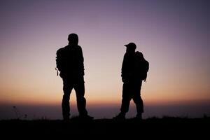 silhouette de promeneur Hommes avec sac à dos rester sur falaise et pense sur le Haut Montagne à le coucher du soleil photo