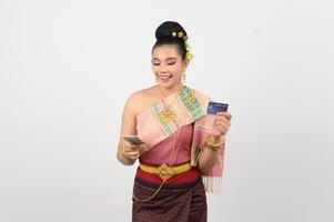 portrait de magnifique thaïlandais femme dans traditionnel Vêtements posant avec billet de banque et crédit carte photo