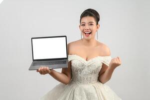 Jeune belle mariée asiatique pose avec un ordinateur portable maquette à la main photo