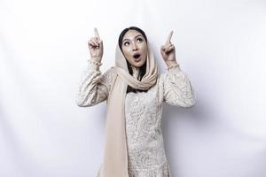 sous le choc asiatique musulman femme portant hijab montrer du doigt à le copie espace sur Haut de son, isolé par blanc Contexte photo