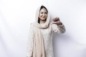 déçu asiatique musulman femme portant une hijab donne les pouces vers le bas main geste de désapprobation, isolé par blanc Contexte photo
