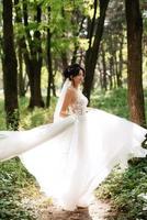 portrait de un élégant la mariée fille sur une chemin dans une à feuilles caduques forêt avec une bouquet photo